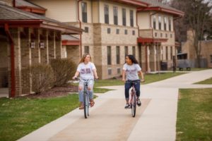 Two female students riding bikes on campus